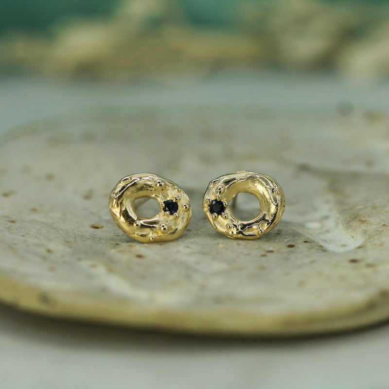 Gold earrings with dark blue sapphires on a textured surface