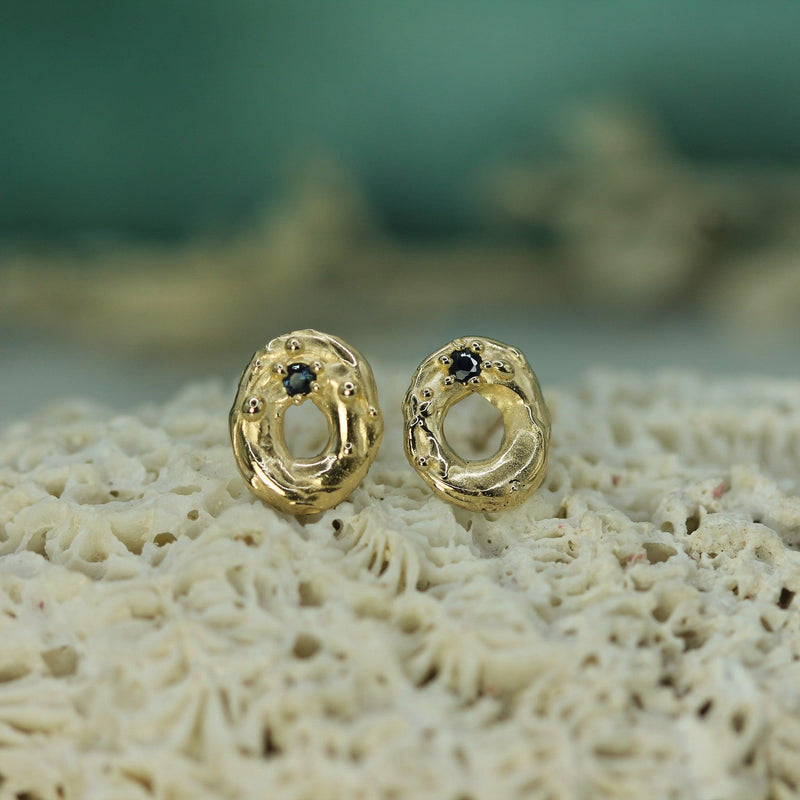 Gold earrings with dark blue sapphires on a textured surface
