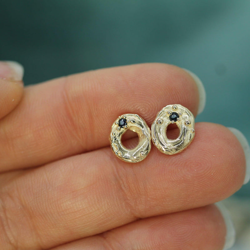 Gold earrings with dark blue sapphires held between fingers against a blurred background