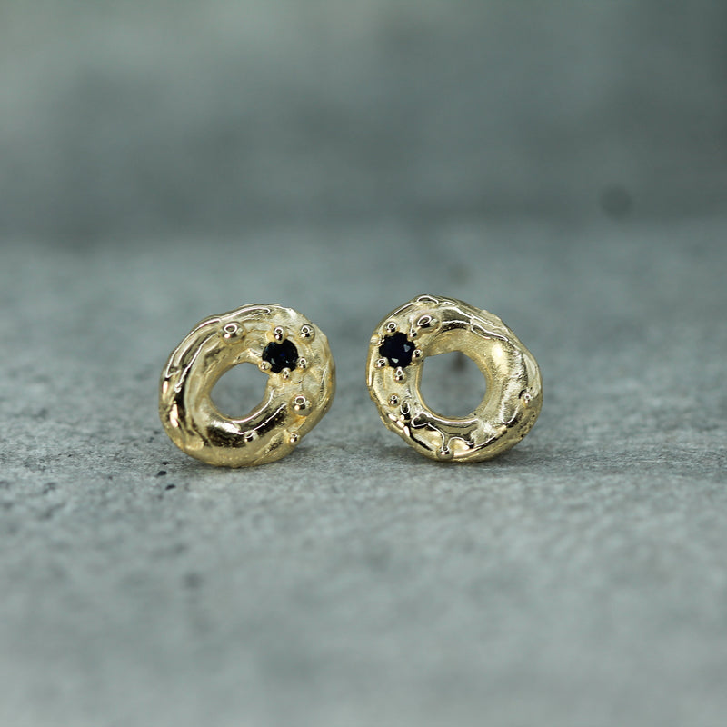 Gold earrings with dark blue sapphire gemstones on a gray surface