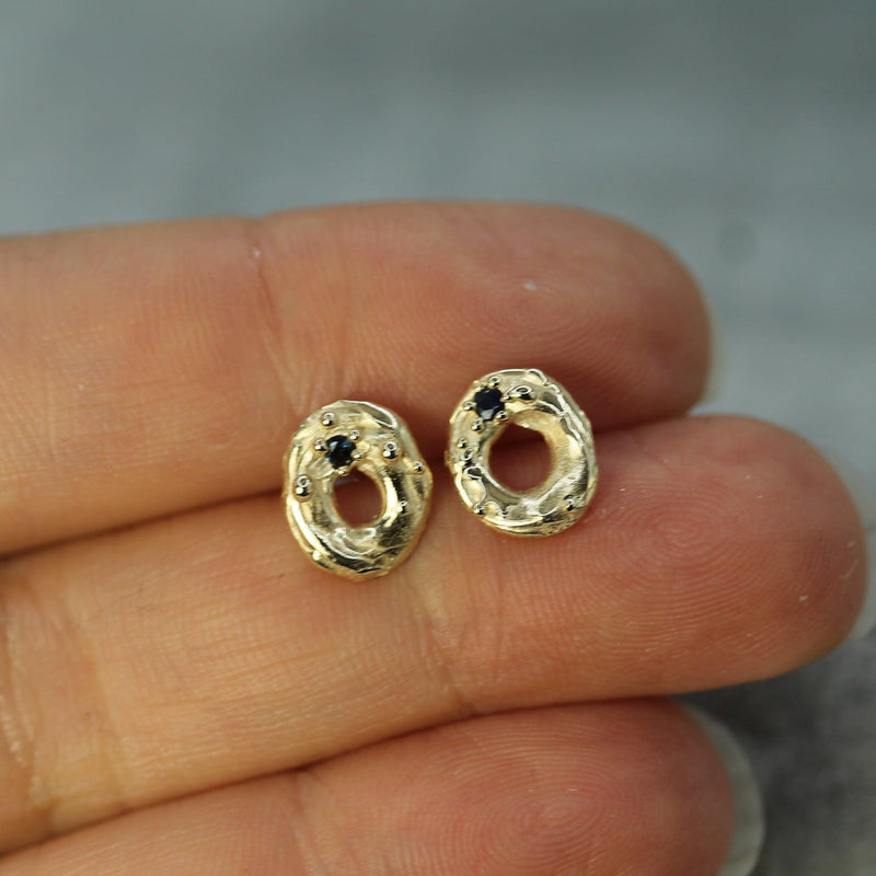 Gold earrings with dark blue sapphires held between fingers against a neutral background