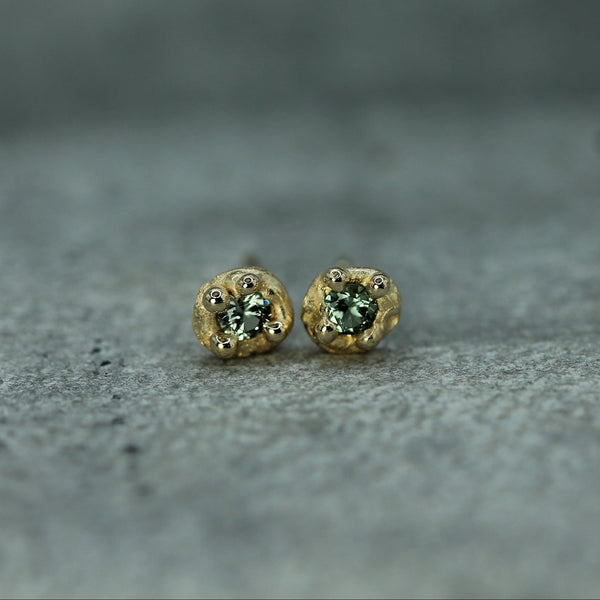 Gold earrings with green sapphires on a gray textured surface