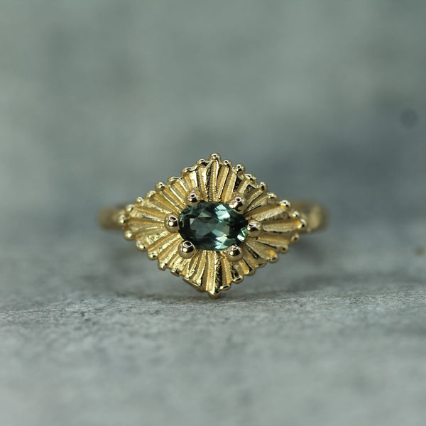 Gold ring with teal sapphires on a gray background