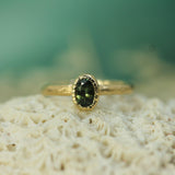 Gold ring with a green sapphire on a textured surface with a blurred green background
