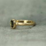Gold ring with a green sapphire on a textured gray background