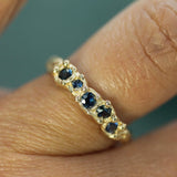 Gold ring with blue sapphires on a finger against a teal background