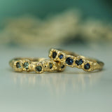 Two gold rings with green and blue sapphires on a blurred background
