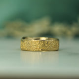 Gold ring with a textured surface on a reflective surface with a blurred natural background